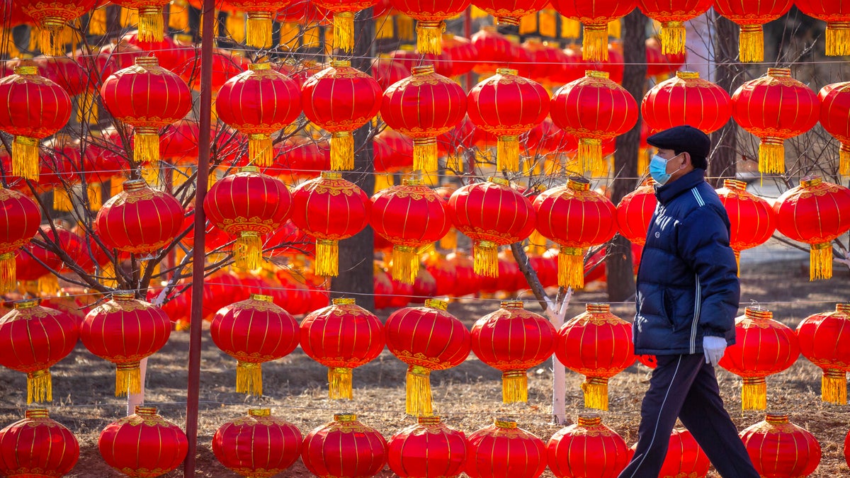 A man wearing a face mask to protect against the spread of the coronavirus walks past a display of lanterns at a public park in Beijing, Tuesday, Jan. 5, 2021. China has designated parts of Hebei province near Beijing as a coronavirus high danger zone after 14 new cases of COVID-19 were found. (AP Photo/Mark Schiefelbein)