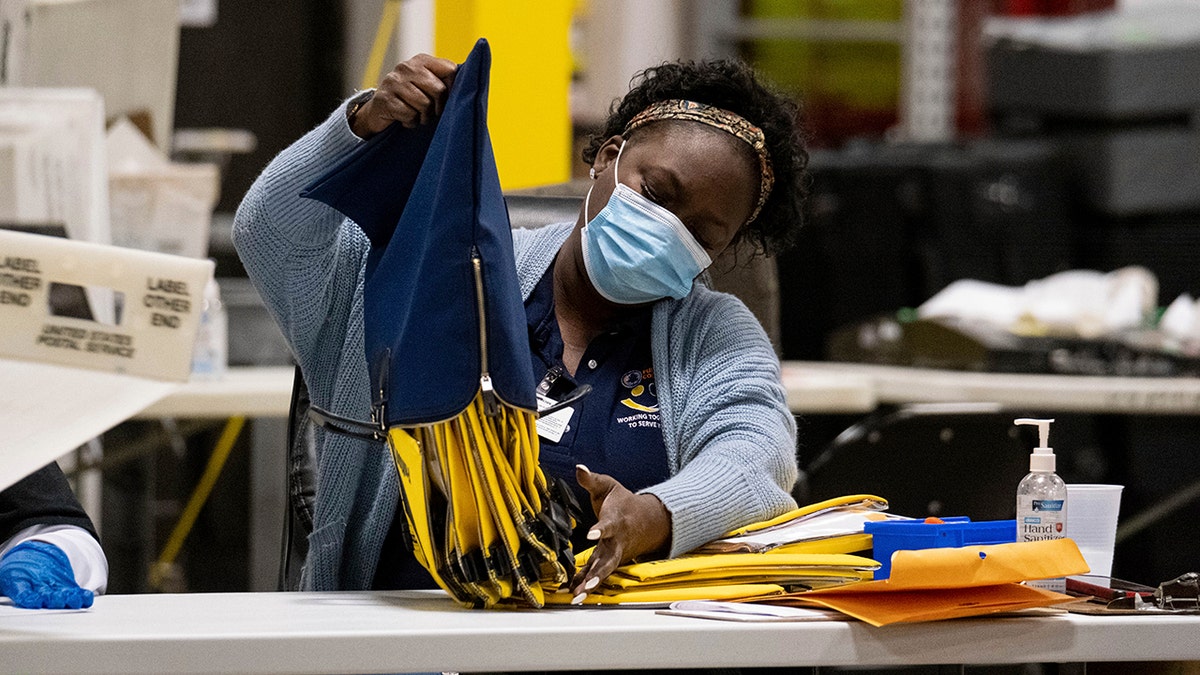 An election worker at the Fulton County Georgia elections warehouse empties a bag following the Senate runoff election in Atlanta on Tuesday, Jan. 5, 2021. (AP Photo/Ben Gray)