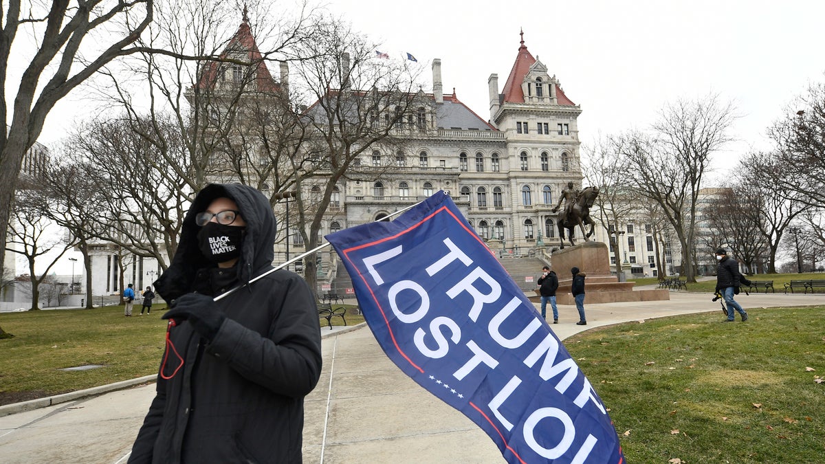 Christina Janowitz of Guilderland, N.Y., from the group "All Of Us' holds a flag while counter-protesting a Trump rally ahead of the inauguration of President-elect Joe Biden and Vice President-elect Kamala Harris at the New York State Capitol Sunday, Jan. 17, 2021, in Albany, N.Y. (AP Photo/Hans Pennink)
