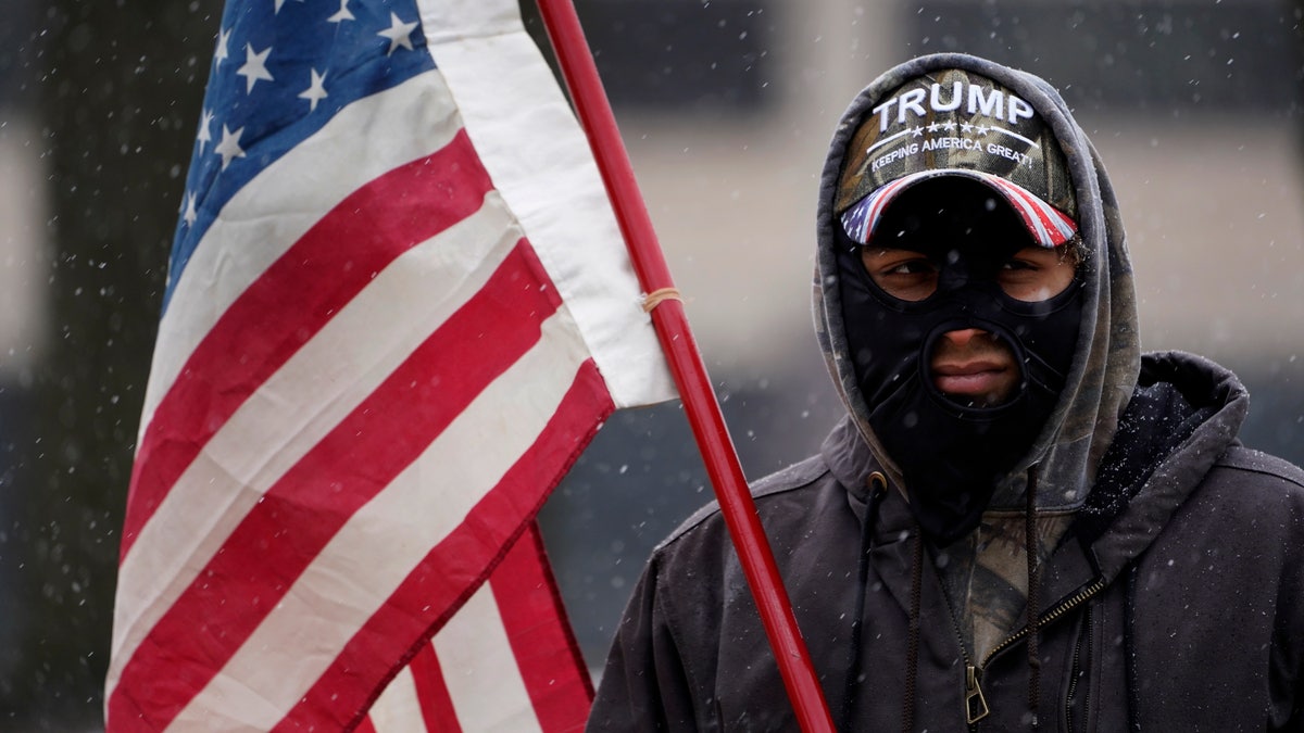 A man stands outside the state capitol wearing a Trump hat with an American flag in Lansing, Mich., Sunday, Jan. 17, 2021. (AP Photo/Paul Sancya)