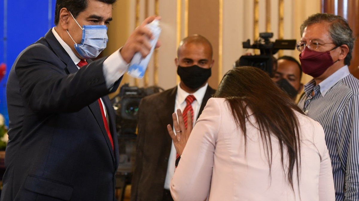 FILE - In this Dec. 8, 2020 file photo, Venezuela's President Nicolas Maduro playfully sprays a journalist with disinfectant as he exits a press conference at Miraflores Presidential Palace in Caracas, Venezuela, amid the new coronavirus pandemic. Attorneys for the cash-strapped government blame the impact of U.S. sanctions for its inability to make an initial $18 million down payment to the United Nations for doses of the U.N.-supplied vaccines, whose deadline has already passed. (AP Photo/Matias Delacroix, File)