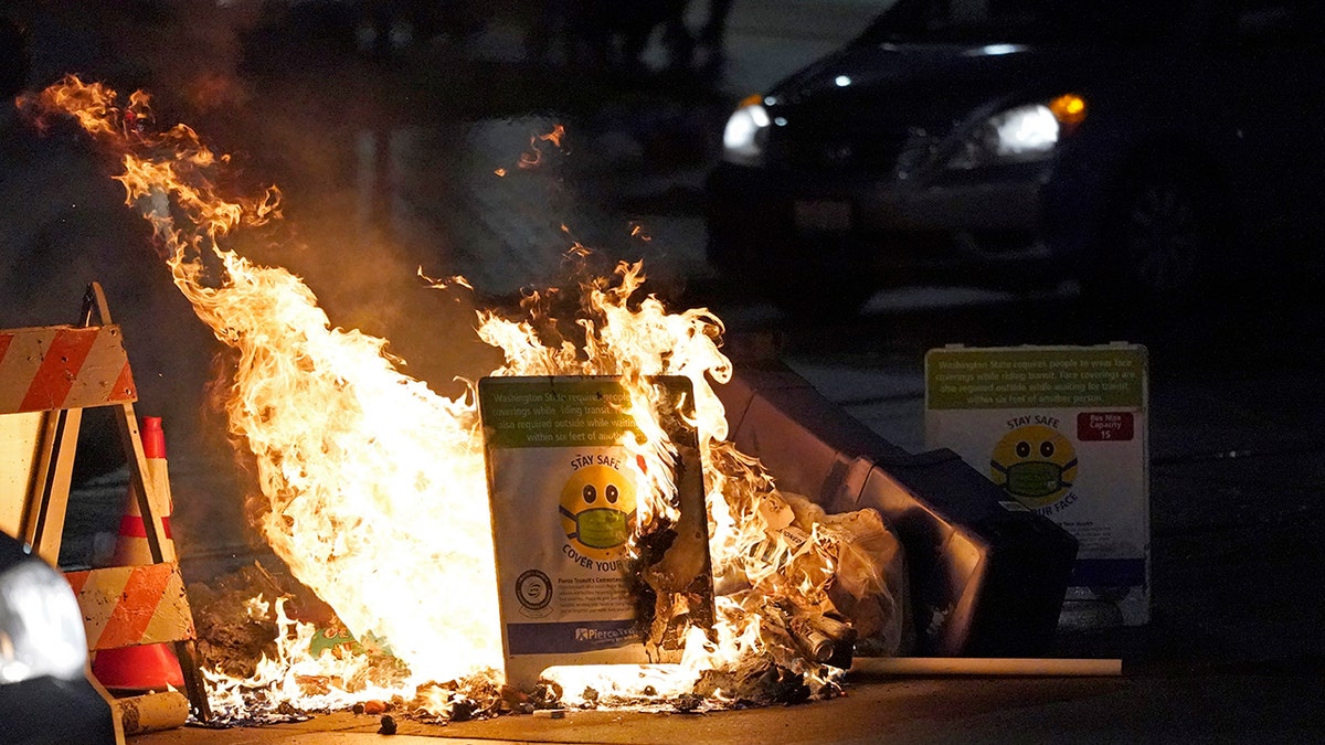 A car drives near burning trash and a COVID-19 mask safety sign during a protest against police brutality, late Sunday, Jan. 24, 2021, in downtown Tacoma, Wash., south of Seattle. (AP Photo/Ted S. Warren)