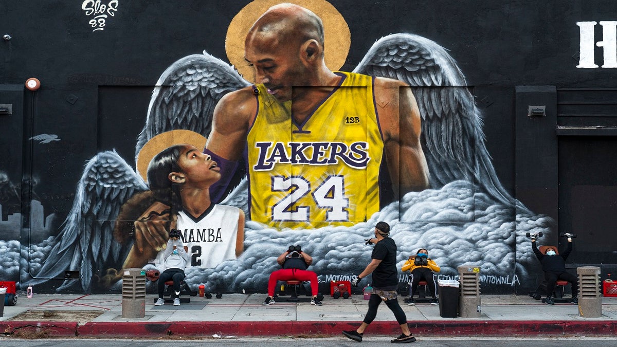 People lift weights on a sidewalk outside the Hardcore Fitness gym, due to COVID-19 restrictions, under a mural honoring NBA star Kobe Bryant and his daughter Gigi near Staples Center in downtown Los Angeles, Monday, Jan. 25, 2021. (AP Photo/Damian Dovarganes)