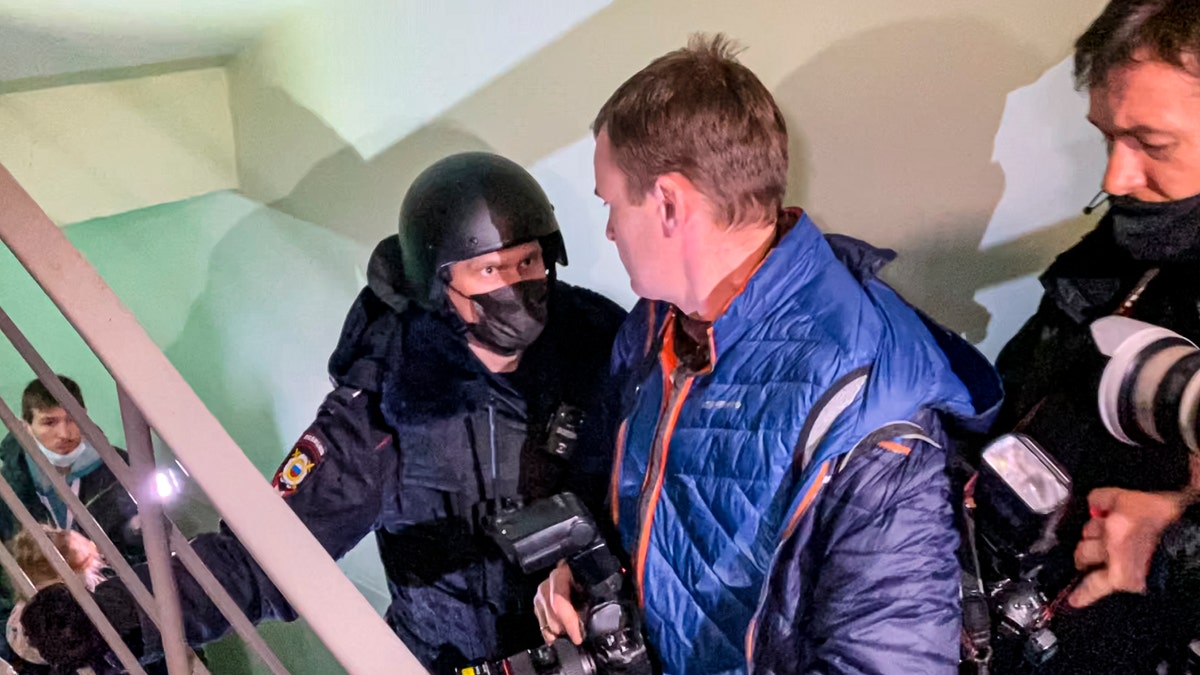 A police officer pushes photographers from a door of the apartment where Oleg Navalny, brother of jailed opposition leader Alexei Navalny lives in Moscow, Russia, Wednesday, Jan. 27, 2021. Police are searching the Moscow apartment of jailed Russian opposition leader Alexei Navalny, another apartment where his wife is living and two offices of his anti-corruption organization. Navalny's aides reported the Wednesday raids on social media. (AP Photo/Mstyslav Chernov)