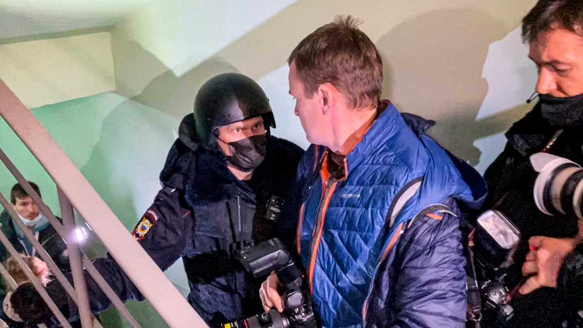 A police officer pushes photographers from a door of the apartment where Oleg Navalny, brother of jailed opposition leader Alexei Navalny lives in Moscow, Russia, Wednesday, Jan. 27, 2021. Police are searching the Moscow apartment of jailed Russian opposition leader Alexei Navalny, another apartment where his wife is living and two offices of his anti-corruption organization. Navalny's aides reported the Wednesday raids on social media. (AP Photo/Mstyslav Chernov)