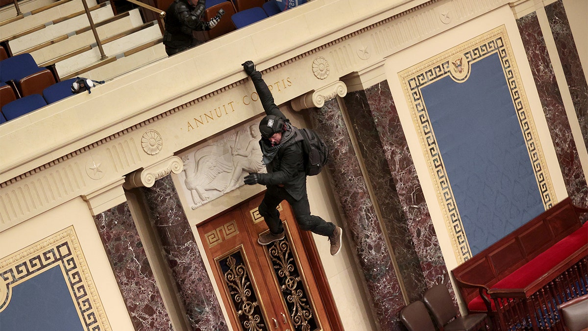 WASHINGTON, DC - JANUARY 06: A protester is seen hanging from the balcony in the Senate Chamber on January 06, 2021 in Washington, DC. Congress held a joint session today to ratify President-elect Joe Biden's 306-232 Electoral College win over President Donald Trump. Pro-Trump protesters have entered the U.S. Capitol building after mass demonstrations in the nation's capital. (Photo by Win McNamee/Getty Images)