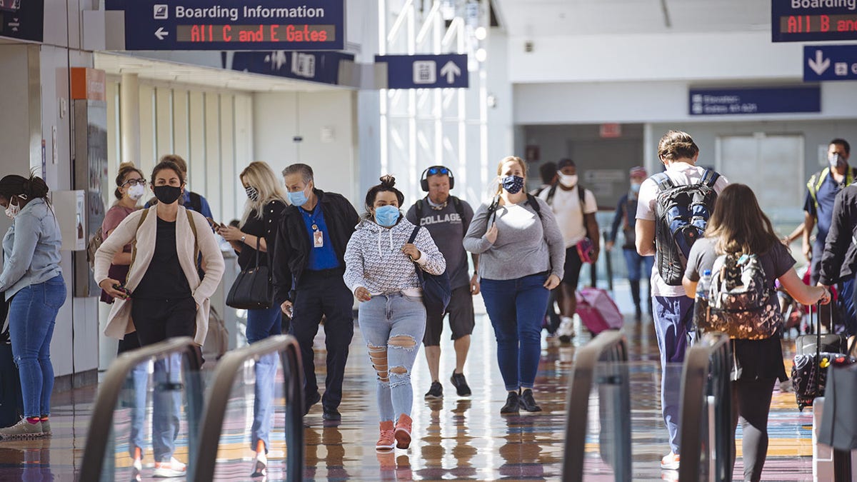 Travelers wearing protective masks walk through Dallas/Fort Worth International Airport (DFW) in Dallas, Texas.