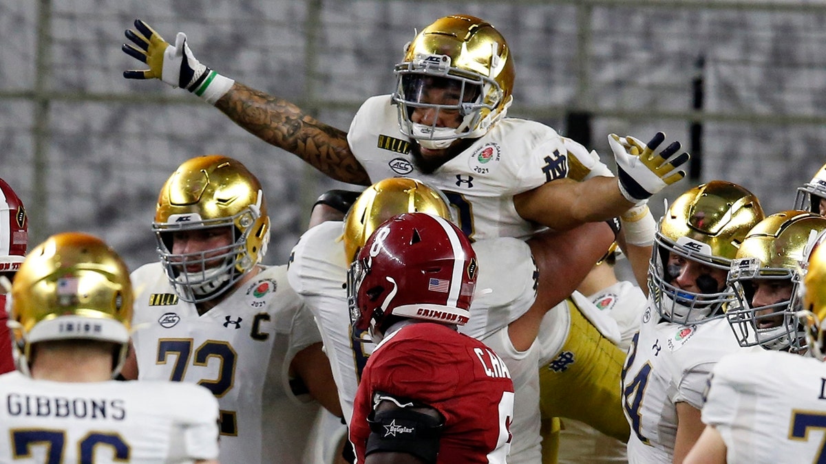 Notre Dame running back Kyren Williams, top, is lifted by offensive lineman Landon Dickerson (69) after Williams' touchdown run as Alabama linebacker Christian Harris (8) looks on in the first half of the Rose Bowl NCAA college football game in Arlington, Texas, Jan. 1. (AP Photo/Roger Steinman)