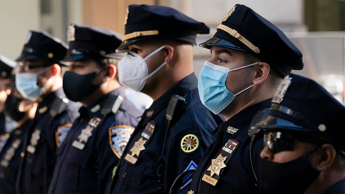 FILE - In this= Oct. 5, 2020, file photo, New York Police Department officers in masks, stand during a service at St. Patrick's Cathedral in New York to honor 46 colleagues who have died due to COVID-19 related illness. New York City Mayor Bill de Blasio and Gov. Andrew Cuomo are again at odds, this time over city police officers' eligibility for COVID-19 vaccines. (AP Photo/Mark Lennihan, File)
