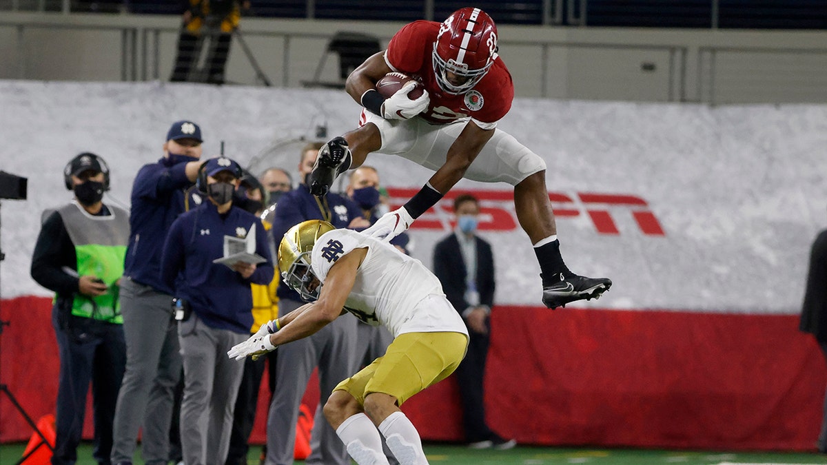 Alabama running back Najee Harris (22) hurdles Notre Dame cornerback Nick McCloud (4) as he carries the ball for a long gain in the first half of the Rose Bowl NCAA college football game in Arlington, Texas, Jan. 1, 2021. (AP Photo/Michael Ainsworth)
