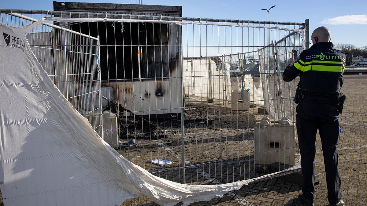 A police officer takes images of a torched coronavirus testing facility in the Dutch fishing village of Urk, Sunday, Jan. 24, 2021, after it was torch Saturday night by rioting youths protesting on the first night of a nation-wide curfew. (AP Photo/Peter Dejong)