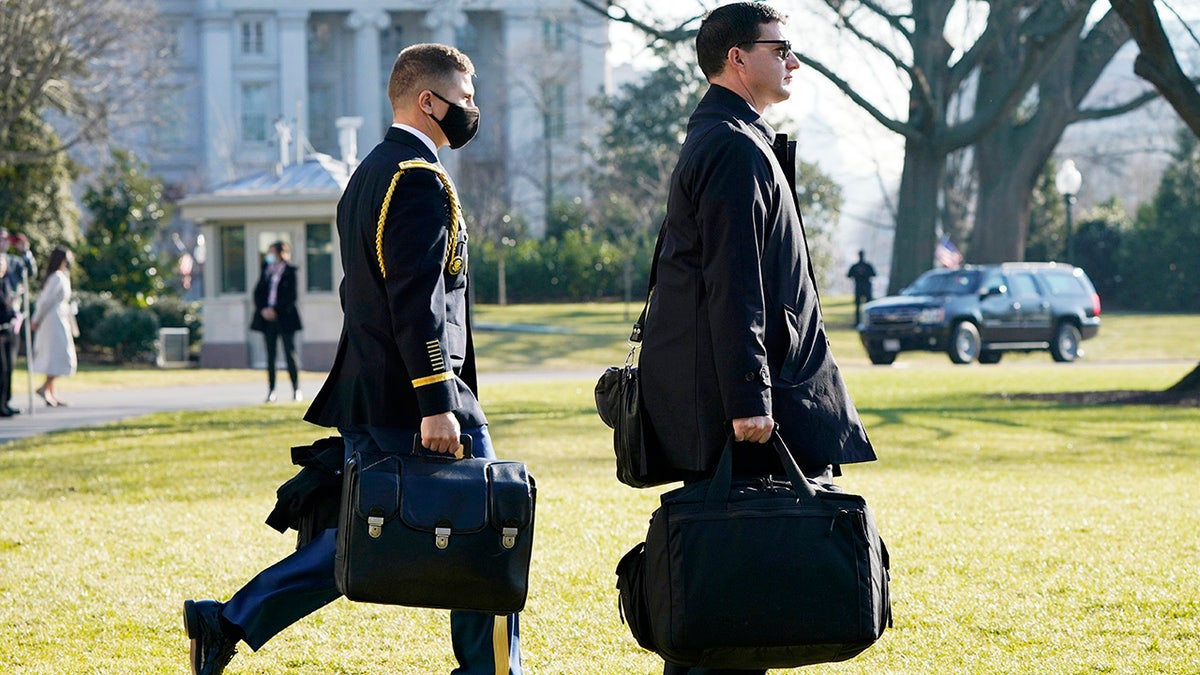 A U.S. military aide, left, carries the "President's emergency satchel," also know as "the football," with the nuclear launch codes, as President Donald Trump walks to board Marine One on the South Lawn of the White House, Tuesday, Jan. 12, 2021, in Washington. (AP Photo/Gerald Herbert )