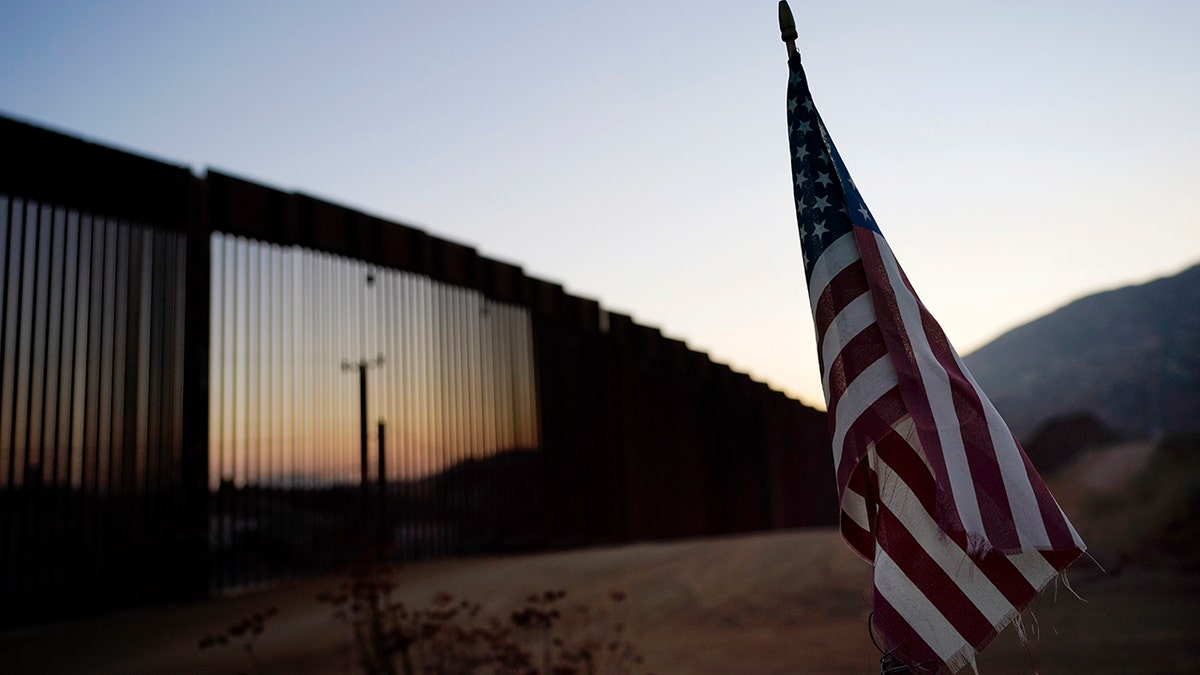 FILE - In this Sept. 24, 2020, file photo a flag sits just north of a new section of the border structure, behind,, near Tecate, Calif. The Trump administration sought to halt migrants from crossing the southwest border through measures that included forcing people seeking asylum to do to so in Mexico or Central America and building about 450 miles of wall. . (AP Photo/Gregory Bull)