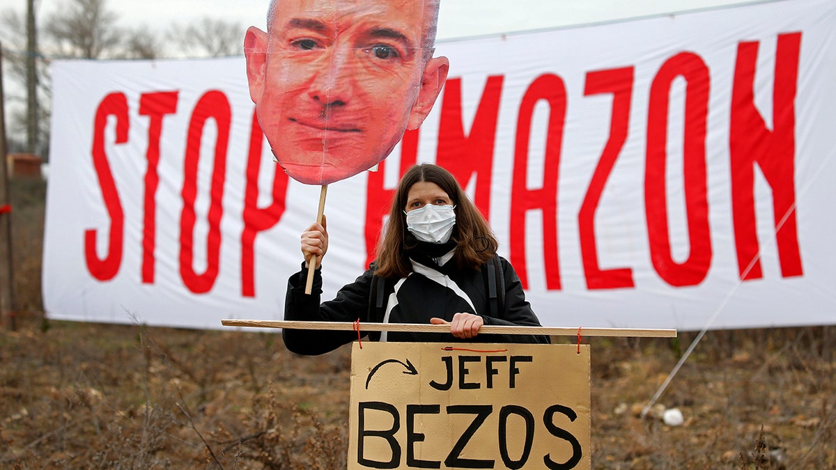 OURNES, FRANCE - JANUARY 30: An opponent holds a cutout sign depicting Amazon CEO Jeff Bezos, in front of a banner reading "Stop Amazon" during a rally against plans to build a giant Amazon warehouse on January 30, 2021 in Fournes (Gard), France. The project to set up a huge Amazon warehouse by the e-commerce giant in Fournes, near the Pont du Gard, faces strong opposition. The demonstrators oppose the "betonization" of 14 hectares of land a few kilometers from the Pont du Gard, (classified as a historical monument as a UNESCO World Heritage Site). (Photo by Chesnot/Getty Images)