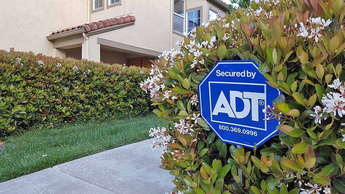 Sign indicating home is secured by ADT alarm system in front of suburban house