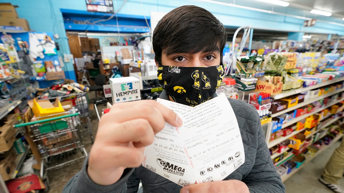Hardik Kalra, of Des Moines, Iowa, poses for a photo with his Mega Millions and Powerball lottery tickets, Tuesday, Jan. 12, 2021, in Des Moines, Iowa. Lottery players have a chance to win the largest jackpots in nearly two years as Tuesday's Mega Millions has grown to an estimated $625 million and Wednesday's Powerball to an estimated $550 million. (AP Photo/Charlie Neibergall)
