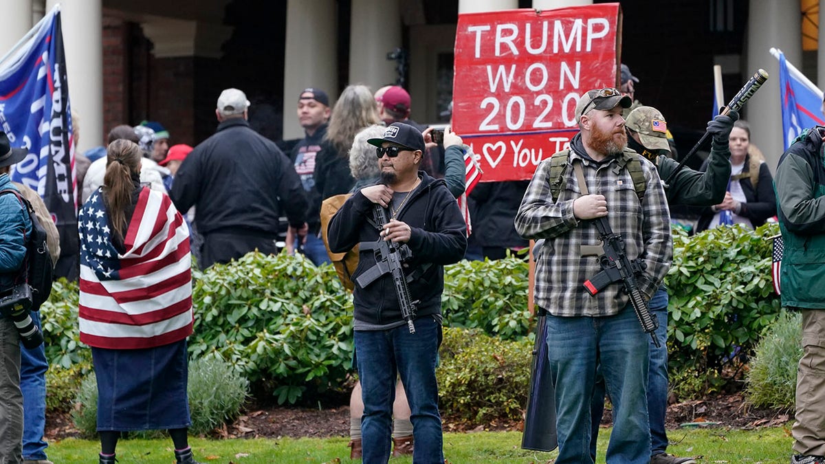 Supporters of President Trump, including those with guns and a bat, stand outside the Governor's Mansion after breaching a perimeter fence, Wednesday, Jan. 6, 2021, at the Capitol in Olympia, Wash. (AP Photo/Ted S. Warren)