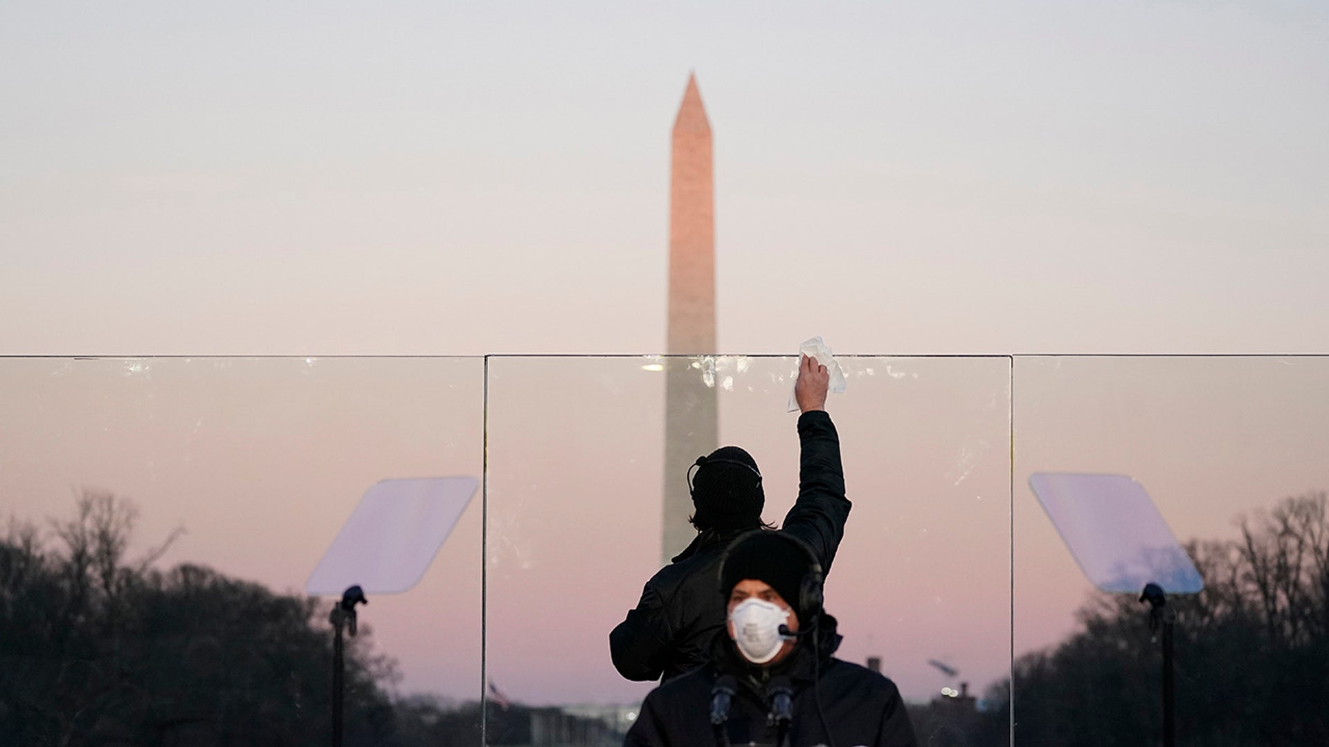 Staff members clean the glass on a protective shield and the podium before President-elect Joe Biden speaks during a COVID-19 memorial, with lights placed around the Lincoln Memorial Reflecting Pool, Tuesday, Jan. 19, 2021, in Washington.