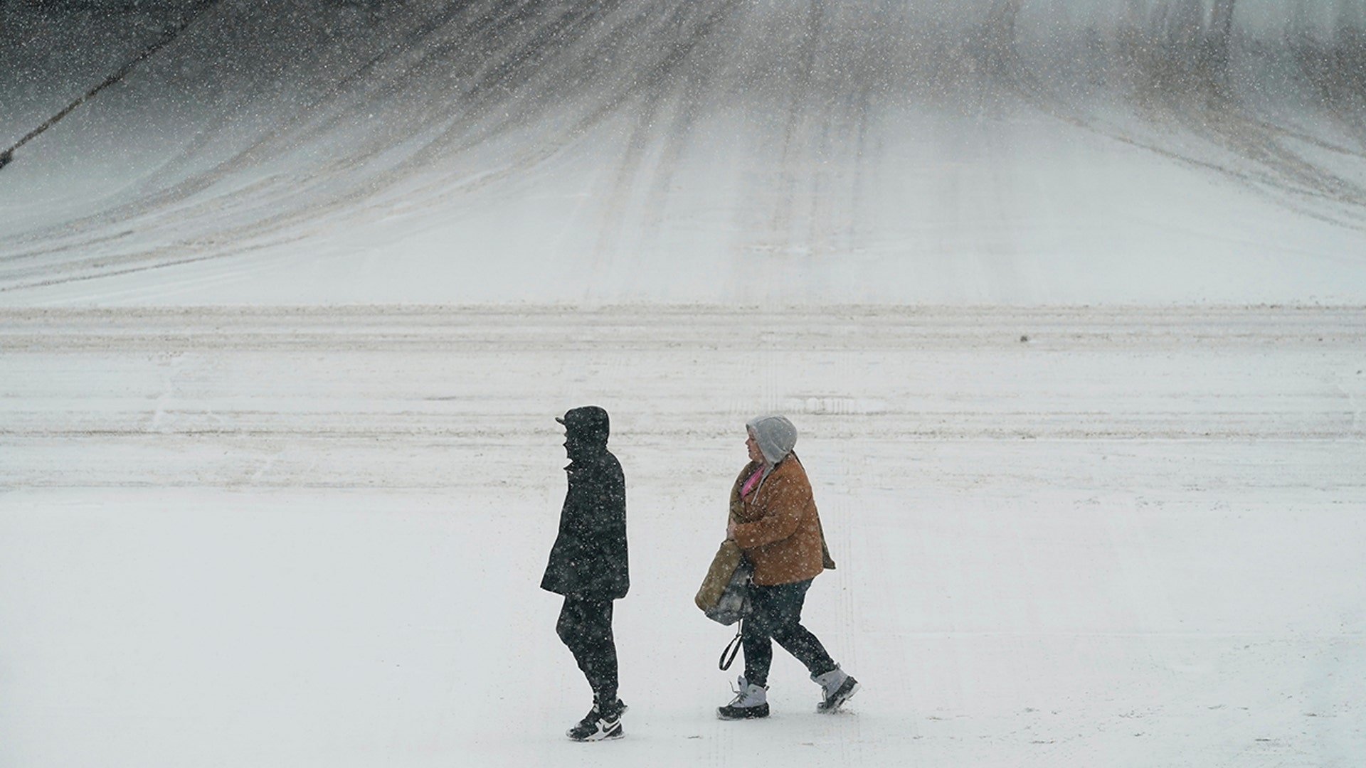Pedestrians cross a snow-covered street, Monday, Jan. 25, 2021, in downtown Des Moines, Iowa. A major winter storm is expected to blanket a large swath of the middle of the country with snow Monday and disrupt travel as more than a foot of snow falls in some areas.
