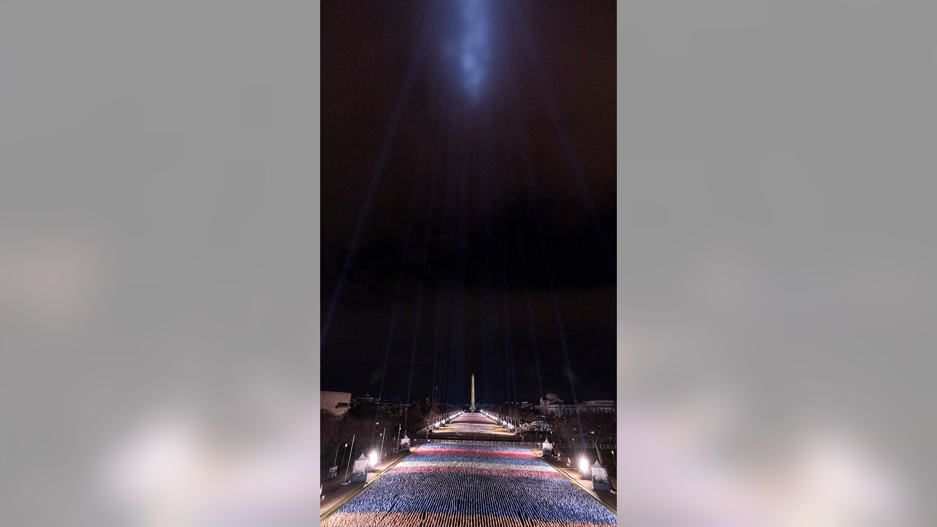 Flags are placed on the National Mall, with the Washington Monument behind them, and lights shine into the sky, ahead of the inauguration of President-elect Joe Biden and Vice President-elect Kamala Harris, Monday, Jan. 18, 2021, in Washington.