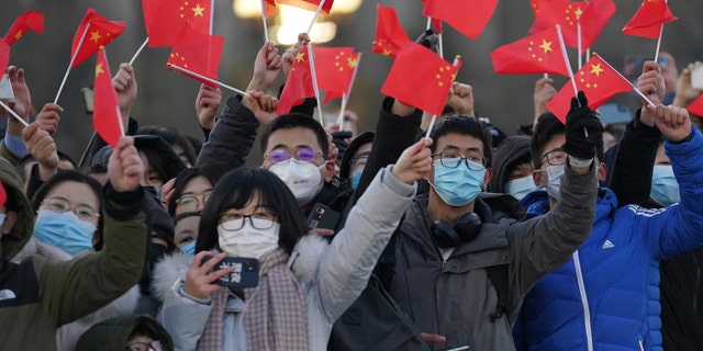 In this photo released by Xinhua News Agency, visitors to Tiananmen Square wave Chinese national flags as they attend the flag raising ceremony on Tiananmen Square in Beijing Friday, Jan. 1, 2021. (Ju Huanzong/Xinhua via AP)