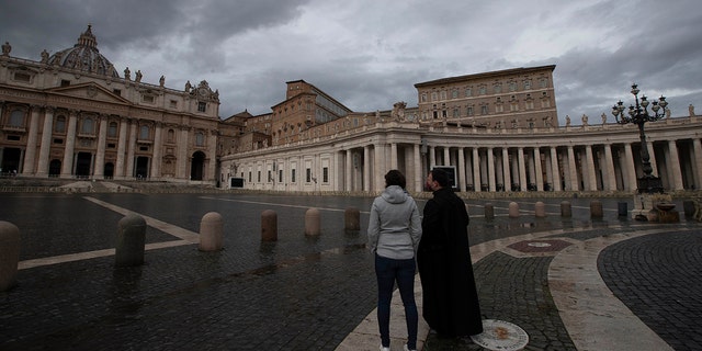 Two people stand in an empty St. Peter's Square at the Vatican as Pope Francis recites the Angelus noon prayer in his studio Friday, Jan. 1, 2021. (AP Photo/Alessandra Tarantino)