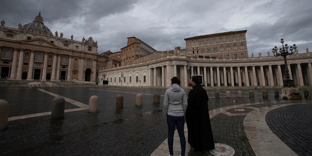 Two people stand in an empty St. Peter's Square at the Vatican as Pope Francis recites the Angelus noon prayer in his studio Friday, Jan. 1, 2021. (AP Photo/Alessandra Tarantino)