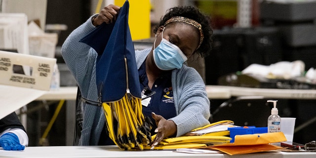 An election worker at the Fulton County Georgia elections warehouse empties a bag following the Senate runoff election in Atlanta on Tuesday, Jan. 5, 2021. (AP Photo/Ben Gray)