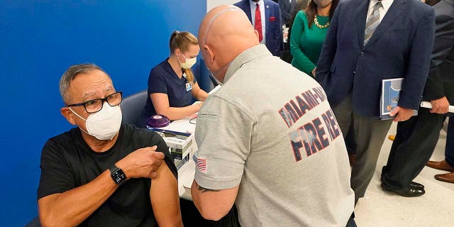 In this Jan. 4, 2021, file photo, Florida Gov. Ron DeSantis, right rear, watches as Carlos Dennis, left, 65, rolls up his sleeve so that Miami-Dade County Fire Rescue paramedic, Capt. Javier Crespo, can administer a COVID-19 vaccine shot at Jackson Memorial Hospital in Miami. 