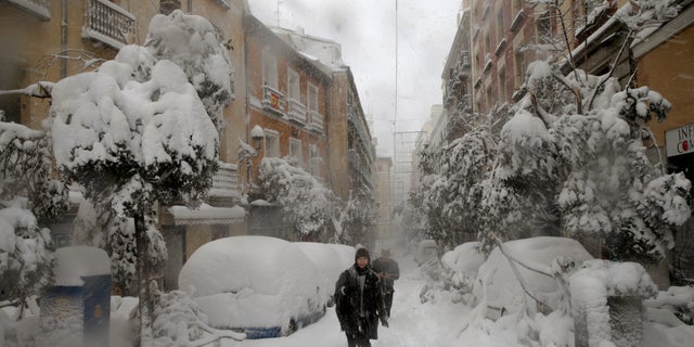 People walk during a heavy snowfall in Madrid, Spain, Saturday, Jan. 9, 2021. An unusual and persistent blizzard has blanketed large parts of Spain with snow, freezing traffic and leaving thousands trapped in cars or in train stations and airports that had suspended all services as the snow kept falling on Saturday. The capital, Madrid, and other parts of central Spain activated for the first time its red weather alert, its highest, and called in the military to rescue people from cars vehicles trapped in everything from small roads to the city's major thoroughfares. (AP Photo/Andrea Comas)