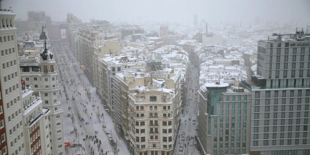People walk during a heavy snowfall in downtown Madrid, Spain, Saturday, Jan. 9, 2021. A persistent blizzard has blanketed large parts of Spain with 50-year record levels of snow, halting traffic and leaving thousands trapped in cars or in train stations and airports that suspended all services as the snow kept falling on Saturday. (AP Photo/Andrea Comas)