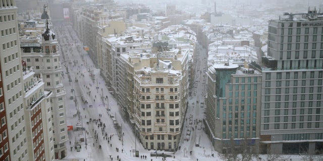 People walk during a heavy snowfall in downtown Madrid, Spain, Saturday, Jan. 9, 2021. A persistent blizzard has blanketed large parts of Spain with 50-year record levels of snow, halting traffic and leaving thousands trapped in cars or in train stations and airports that suspended all services as the snow kept falling on Saturday. (AP Photo/Andrea Comas)