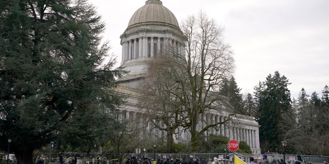 A group of anti-fascist protesters dressed in black make a brief stop outside a perimeter fence being watched by National Guard members and Washington State Patrol troopers, Sunday, Jan. 10, 2021, at the Capitol in Olympia, Wash. Washington Gov. Jay Inslee activated members of the National Guard this week to work with the Washington State Patrol to protect the Capitol campus. The group, part of a larger protest that was taking place in downtown Olympia, left after several minutes of exchanging words with troopers and guard members. (AP Photo/Ted S. Warren)