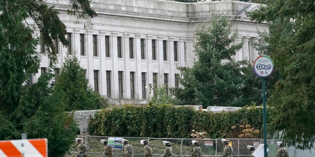 National Guard members march near a perimeter fence, Sunday, Jan. 10, 2021, at the Capitol in Olympia, Wash. Washington Gov. Jay Inslee activated members of the National Guard this week to work with the Washington State Patrol to protect the Capitol campus. A small rally with speakers, flags and signs representing several groups was held near the fence Sunday, but most attendees had left by early evening. (AP Photo/Ted S. Warren)