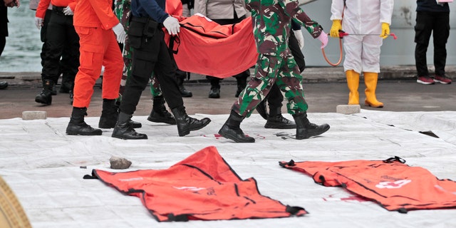 Rescuers carry a body bag of items recovered from the Sriwijaya Air passenger jet crash at Tanjung Priok Port, Tuesday, Jan. 12, 2021. Indonesian navy divers were searching through plane debris and seabed mud Tuesday looking for the black boxes of a Sriwijaya Air jet that nosedived into the Java Sea over the weekend with 62 people aboard. (AP Photo/Dita Alangkara)