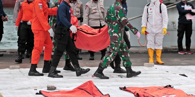 Rescuers carry a body bag of items recovered from the Sriwijaya Air passenger jet crash at Tanjung Priok Port, Dinsdag, Jan.. 12, 2021. Indonesian navy divers were searching through plane debris and seabed mud Tuesday looking for the black boxes of a Sriwijaya Air jet that nosedived into the Java Sea over the weekend with 62 mense aan boord. (AP Photo/Dita Alangkara)