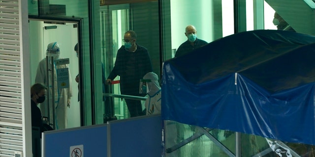 Passengers arriving on a flight from Singapore are processed by staff in protective clothing and directed toward a covered walkway to a separate exit from the airport terminal in Wuhan in central China's Hubei province on Thursday, Jan. 14, 2021. Chinese state media reported that a WHO team arrived in Wuhan on Thursday to research the origins of the coronavirus. (AP Photo/Ng Han Guan)