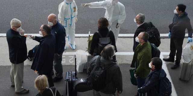 A worker in protective coverings directs members of the World Health Organization team on their arrival at the airport in Wuhan in central China's Hubei province on Thursday, Jan. 14, 2021. A global team of researchers arrived Thursday in the Chinese city where the coronavirus pandemic was first detected to conduct a politically sensitive investigation into its origins amid uncertainty about whether Beijing might try to prevent embarrassing discoveries. (AP Photo/Ng Han Guan)