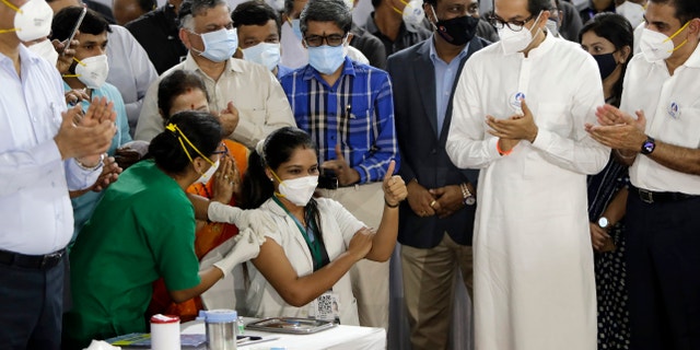 Madhura Patil, a health worker, gestures as she receives COVID-19 vaccine in the presence of Uddhav Thackeray, standing in white dress, Chief Minister of Maharashtra State in Mumbai, India, Saturday, Jan. 16, 2021. India started inoculating health workers Saturday in what is likely the world's largest COVID-19 vaccination campaign, joining the ranks of wealthier nations where the effort is already well underway. (AP Photo/Rajanish Kakade)