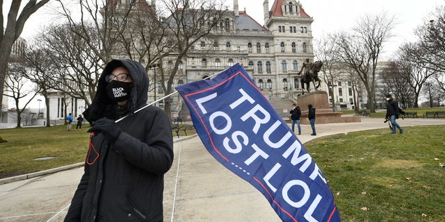 Christina Janowitz of Guilderland, N.Y., from the group "All Of Us' holds a flag while counter-protesting a Trump rally ahead of the inauguration of President-elect Joe Biden and Vice President-elect Kamala Harris at the New York State Capitol Sunday, Jan. 17, 2021, in Albany, N.Y. (AP Photo/Hans Pennink)