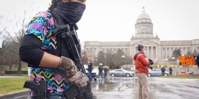 A Black Lives Matter activist carrying a semi-automatic rifle walks outside at the Capitol building in Frankfort, Ky., Wednesday, Jan 17, 2021. The Capitol, the Capitol complex and surrounding grounds have been closed. (AP Photo/Bryan Woolston)
