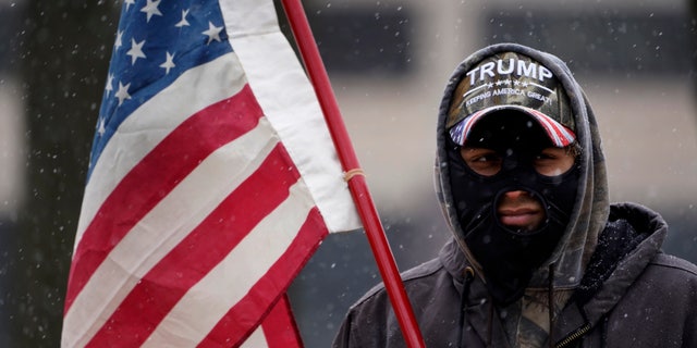 A man stands outside the state capitol wearing a Trump hat with an American flag in Lansing, Mich., Sunday, Jan. 17, 2021. (AP Photo/Paul Sancya)