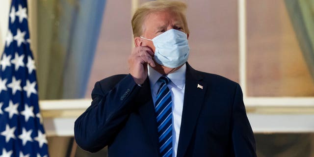 In this Oct. 5, 2020, file photo, President Donald Trump removes his mask as he stands on the Blue Room Balcony upon returning to the White House in Washington, after leaving Walter Reed National Military Medical Center, in Bethesda, Md. Trump announced he tested positive for COVID-19 on Oct. 2. (AP Photo/Alex Brandon, File)