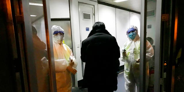 FILE: Health Officials in hazmat suits wait at the gate to check body temperatures of passengers arriving from the city of Wuhan, at the airport in Beijing, China. 