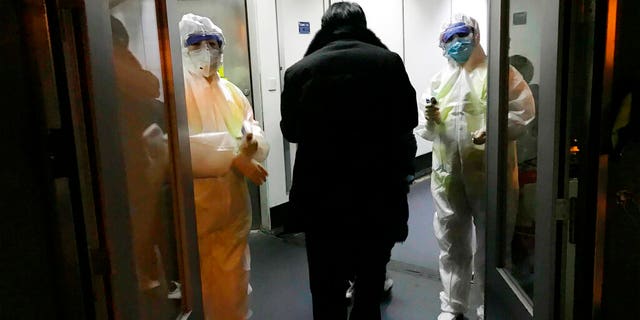 FILE: Health Officials in hazmat suits wait at the gate to check body temperatures of passengers arriving from the city of Wuhan, at the airport in Beijing, China.