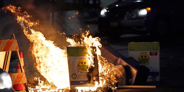 A car drives near burning trash and a COVID-19 mask safety sign during a protest against police brutality, late Sunday, Jan. 24, 2021, in downtown Tacoma, Wash., south of Seattle. (AP Photo/Ted S. Warren)