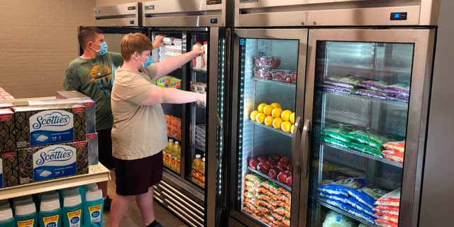 Hunter Weertman, 16, left, works alongside a fellow student to stock the refrigerator in the student-led free grocery store at Linda Tutt High School. (Anthony Love via AP)