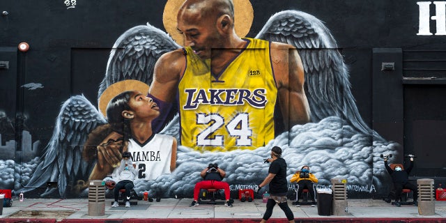 People lift weights on a sidewalk outside the Hardcore Fitness gym, due to COVID-19 restrictions, under a mural honoring NBA star Kobe Bryant and his daughter Gigi near Staples Center in downtown Los Angeles, Monday, Jan. 25, 2021. (AP Photo/Damian Dovarganes)