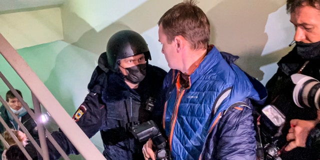 A police officer pushes photographers from a door of the apartment where Oleg Navalny, brother of jailed opposition leader Alexei Navalny lives in Moscow, Russia, Wednesday, Jan. 27, 2021. Police are searching the Moscow apartment of jailed Russian opposition leader Alexei Navalny, another apartment where his wife is living and two offices of his anti-corruption organization. Navalny's aides reported the Wednesday raids on social media. (AP Photo/Mstyslav Chernov)