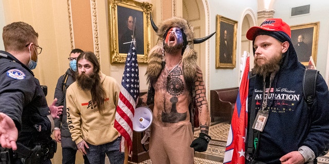 Dans cette photo d'archive du mercredi 6 janvier 2021, des partisans du président Donald Trump, dont Jacob Chansley, au centre avec fourrure et chapeau à cornes, sont confrontés à des agents de la police du Capitole devant la salle du Sénat à l'intérieur du Capitole à Washington.  Une vidéo montrait Chansley en train de diriger d'autres personnes dans une prière à l'intérieur de la salle du Sénat.  (Photo AP / Manuel Balce Ceneta)